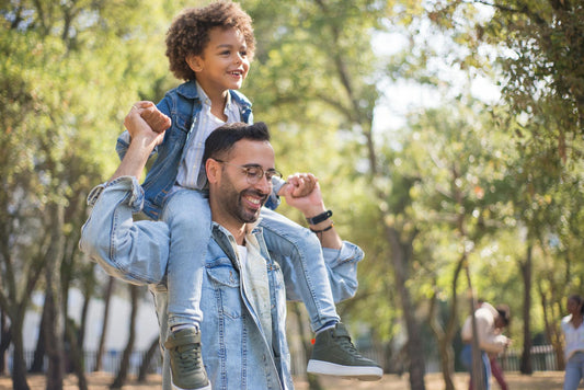 Smiling father carrying his young son on his shoulders during a sunny walk in the park, representing joyful Father’s Day moments and thoughtful gift ideas.