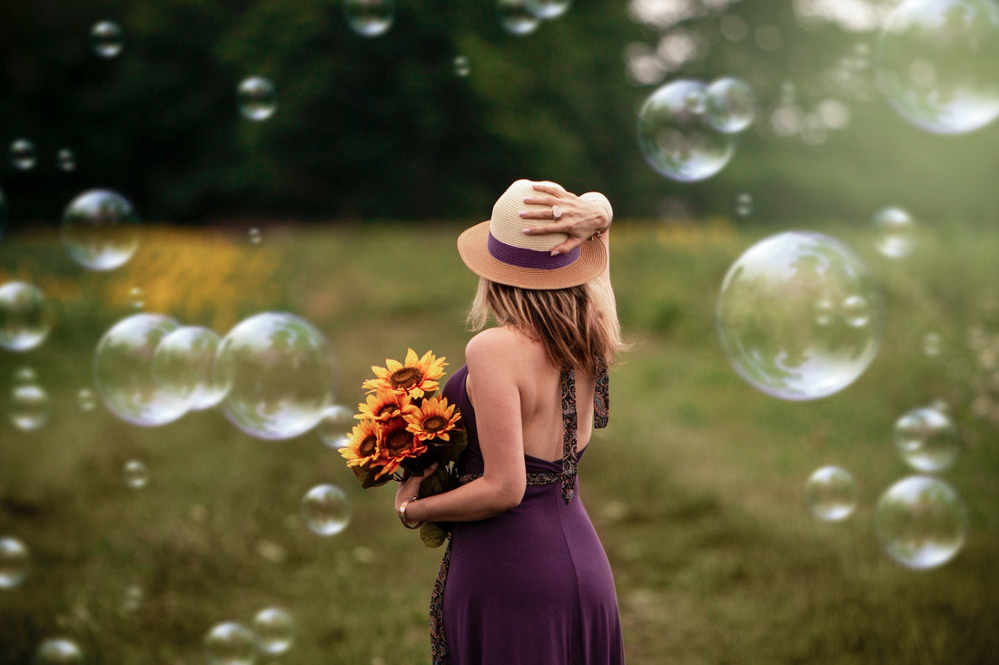 Woman in a purple dress in a grass field with bubbles in the air