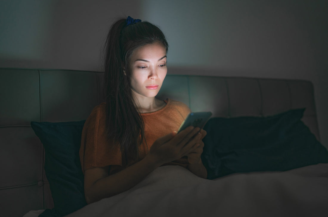 Woman looking at phone late at night, illustrating revenge bedtime procrastination and the struggle to unwind after a busy day