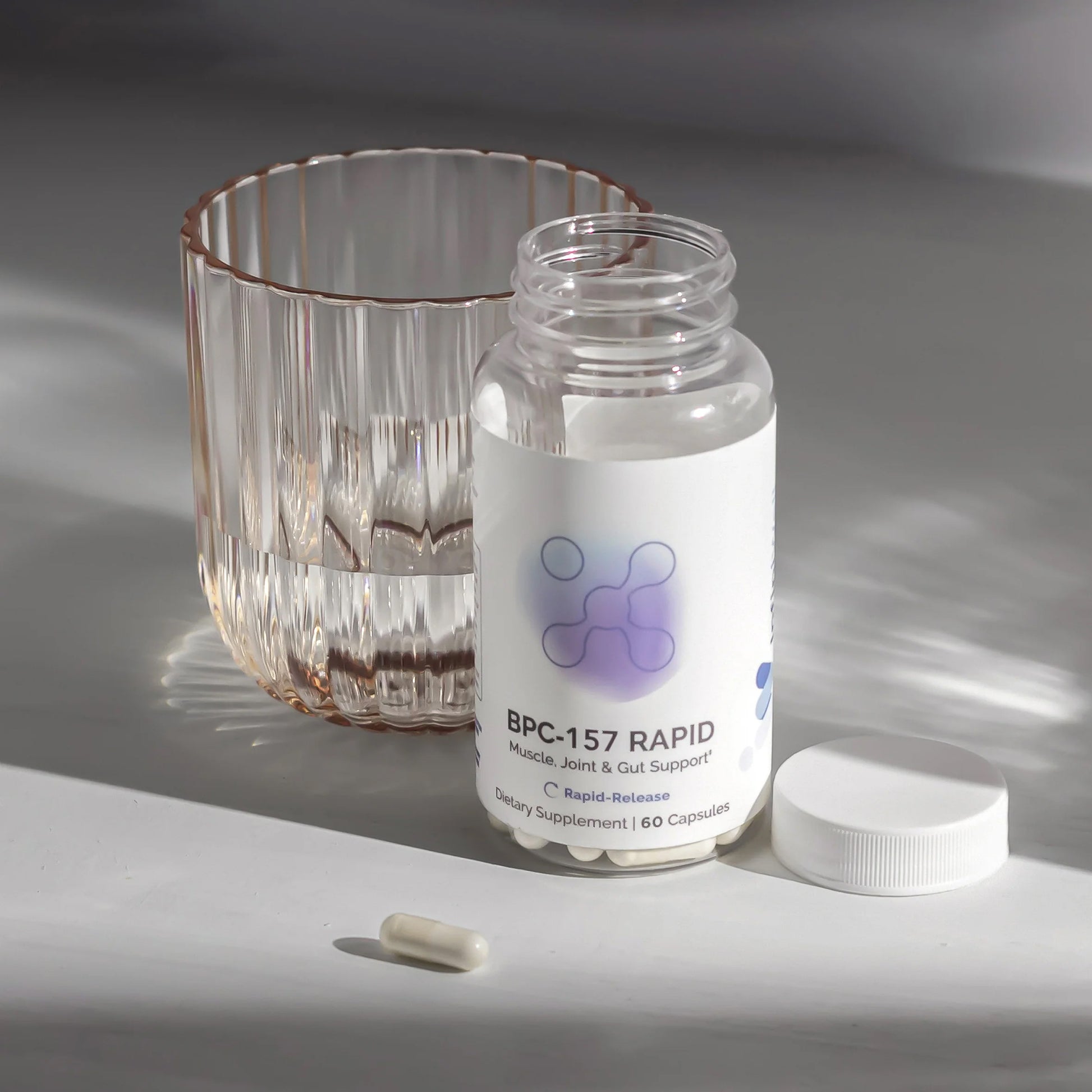 Bottle of BPC-157 Rapid supplement with a glass of water and a pill on a white surface