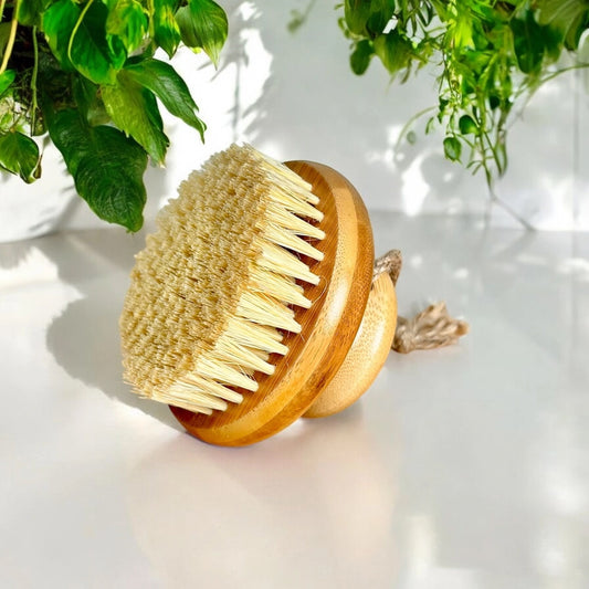 Bamboo dry body brush with natural bristles on a light surface with greenery in the background
