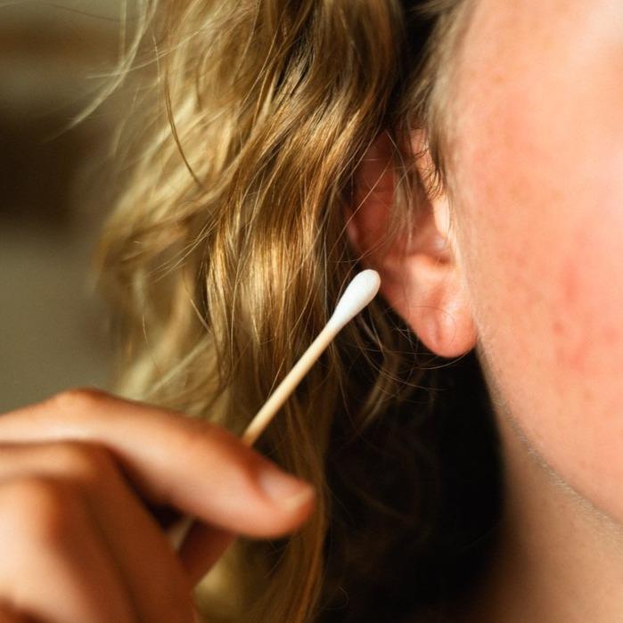 Person cleaning ear with bamboo and cotton swab