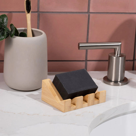 Bamboo soap dish with Black soap bar on it and bathroom fixtures in the background.