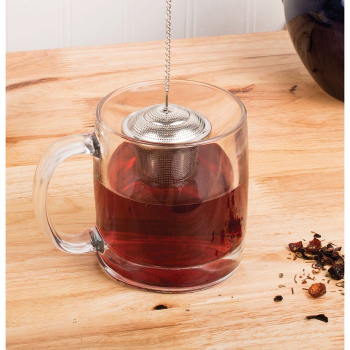 Clear glass mug with tea and a stainless steel barrel infuser on a wooden surface