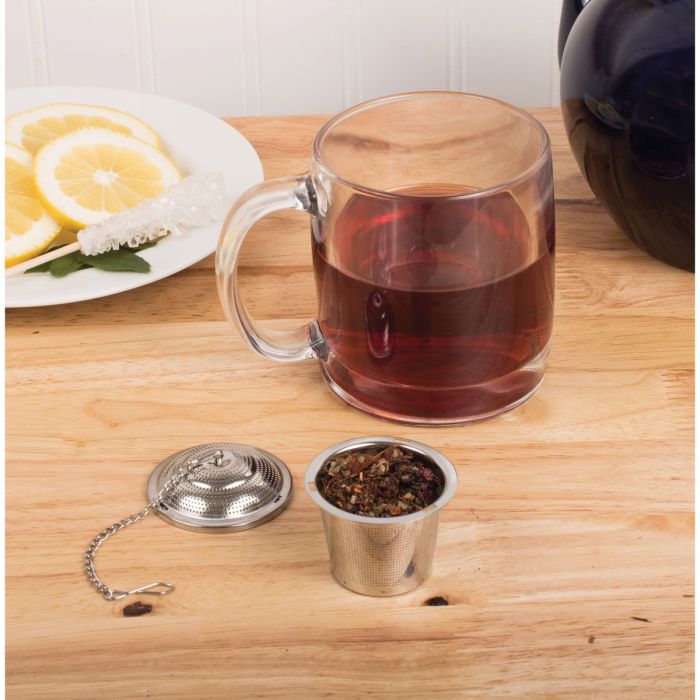 Clear glass mug with hot tea, metal tea ball, and lemon slices on a wooden surface.