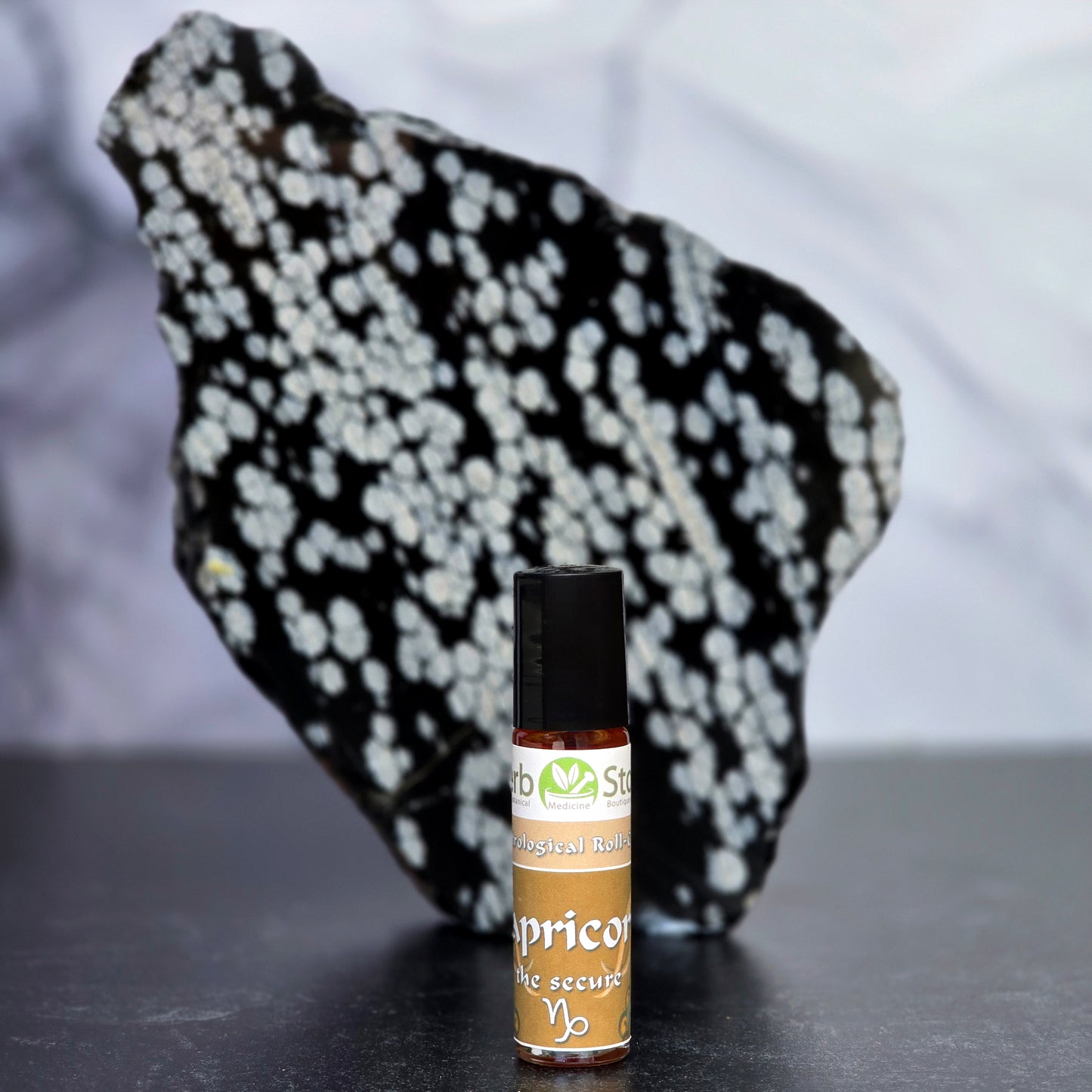 Capricorn Roll-On Astrological Oil bottle on a dark surface with a snowflake obsidian crystal