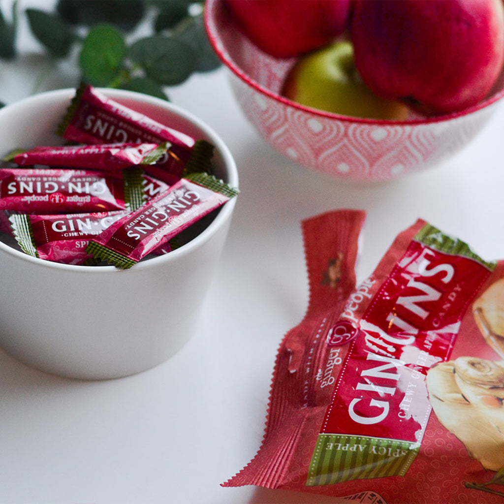 The Ginger People Gin Gins Chewy Ginger Apple Candy in a cup with a bowl of red apples