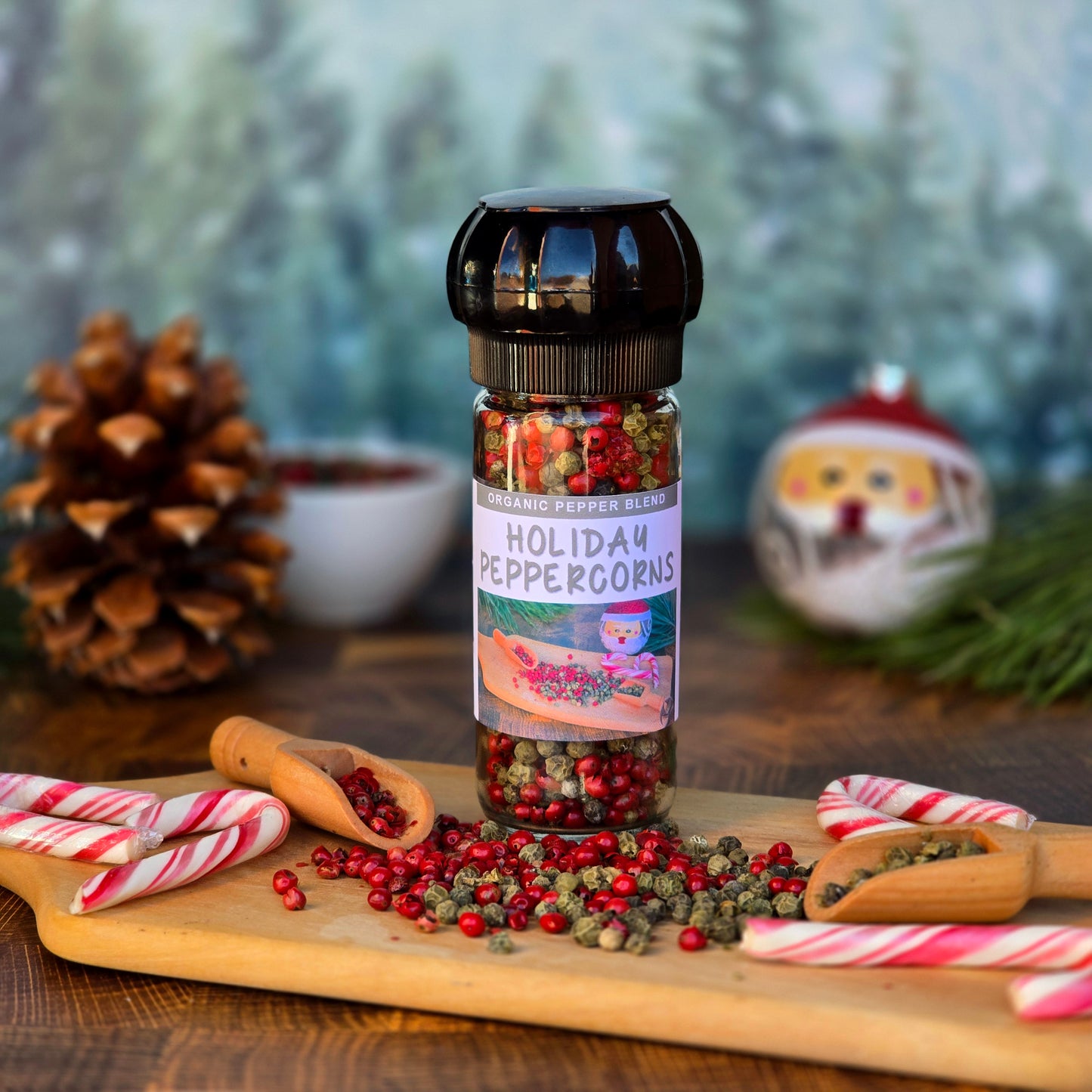 Holiday Peppercorns in a glass bottle with a grinder lid, surrounded by pine needles & cones, candy canes and pink and green peppercorns.
