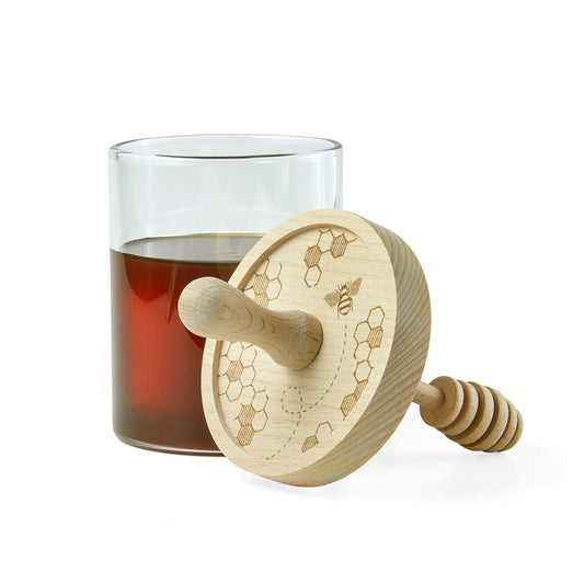 Wooden honey dipper with a glass of honey on a white background