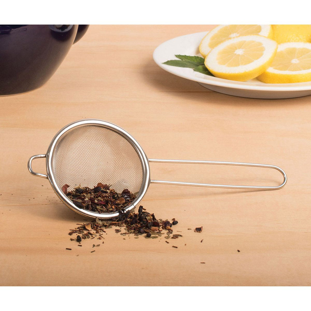 Tea strainer with loose tea leaves on a wooden surface with lemon slices in the background