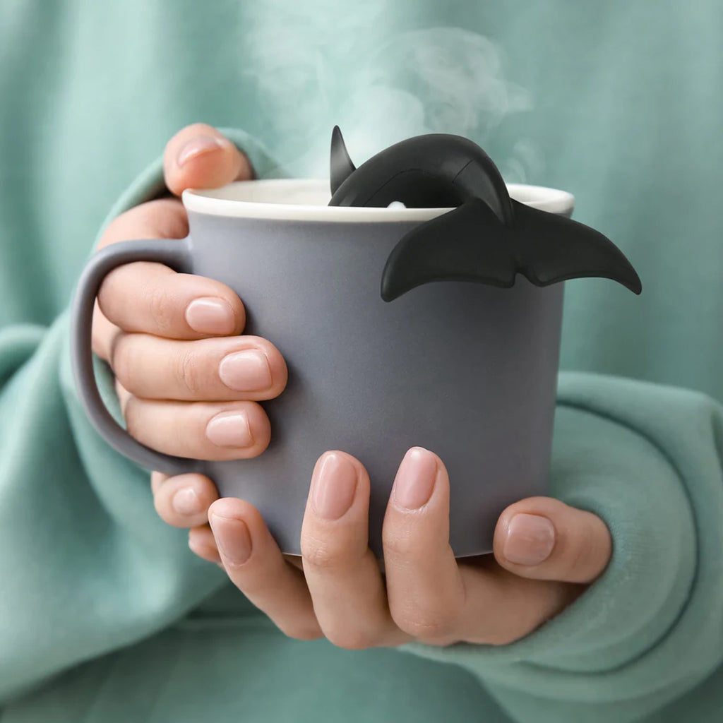 Person holding a gray mug with a whale's tail fin infuser against a green sweatshirt