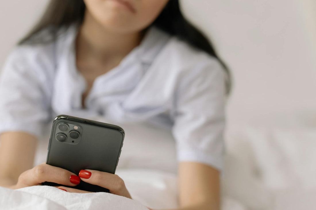 Woman lying in bed scrolling on a smartphone, illustrating doom-scrolling and digital overload.