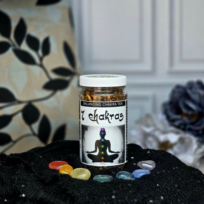 7 Chakras Balancing Herbal Tea jar surrounded by 7 chakra stones on a black cloth with flowers in the background
