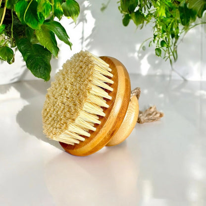 Bamboo dry body brush with natural bristles on a light surface with greenery in the background