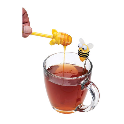 Honey dipper shaped like a bee being used to add honey into a glass of tea with a bee tea infuser.