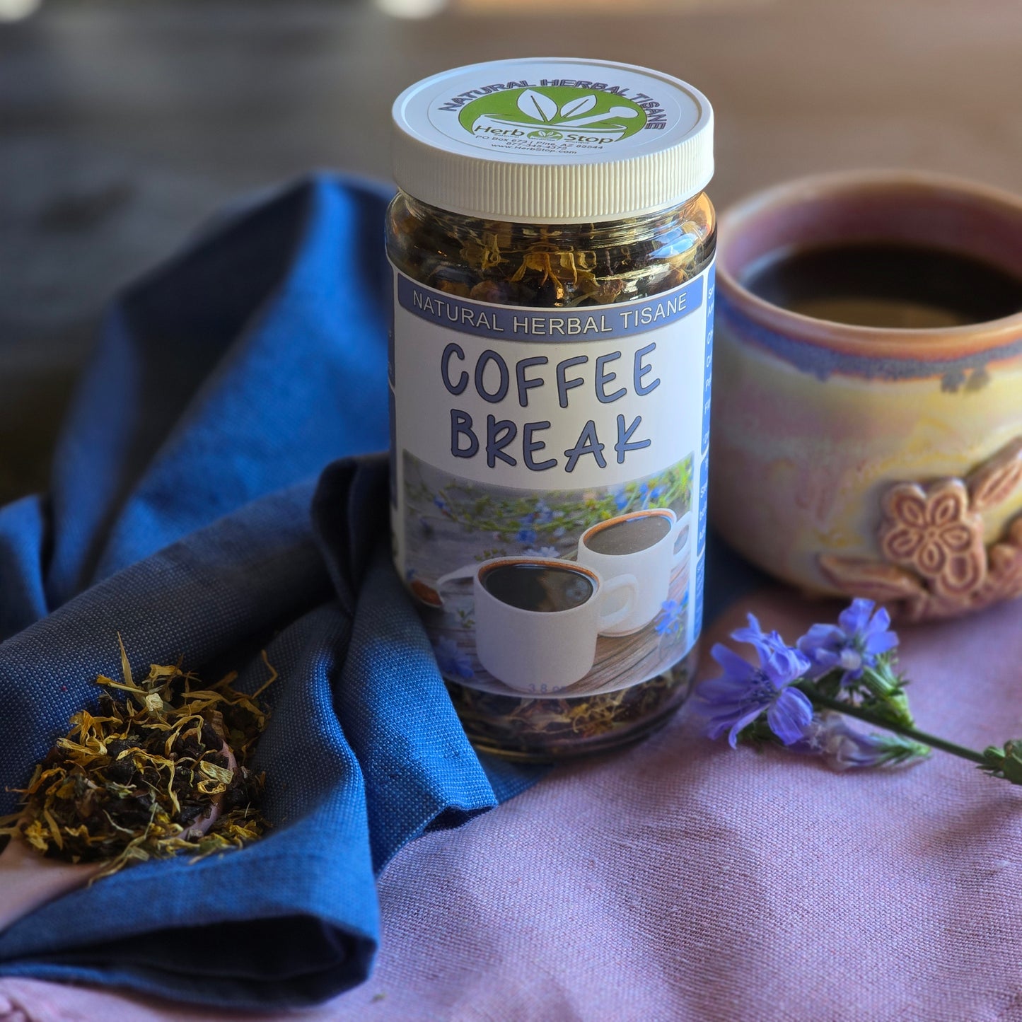 Coffee Break Herbal Tea on a purple tablecloth with chicory flowers and a teacup with tea surrounded by a blue napkin.