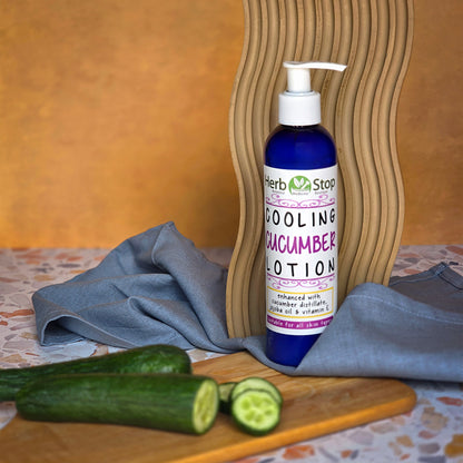 Bottle of Herb Stop Cooling Cucumber Lotion on a wooden surface with cucumbers and a towel.