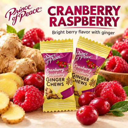 Two packages of Prince of Peace Cranberry Raspberry Ginger Chews are displayed in the center, surrounded by fresh cranberries, raspberries, ginger roots, and sliced ginger on a light surface. The background is a soft beige with promotional text reading 'Prince of Peace' and 'CRANBERRY RASPBERRY'.