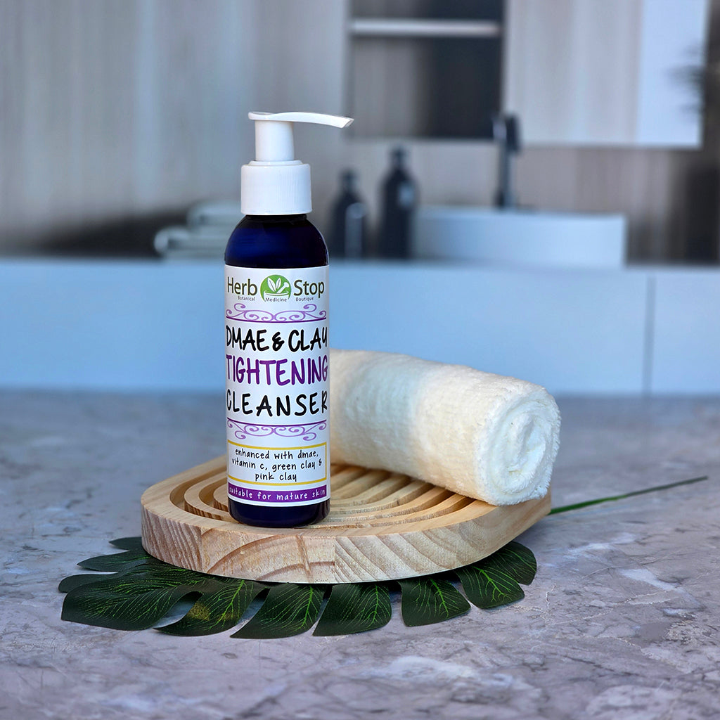 Bottle of Herb Stop DMAE & Clay Tightening Cleanser on a wooden coaster with a towel in a bathroom setting