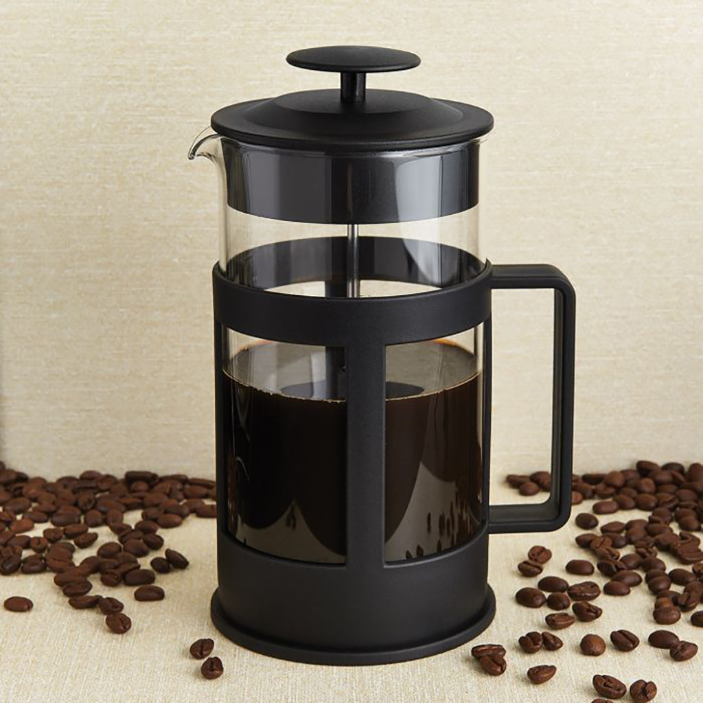 French press with coffee and scattered coffee beans on a beige background