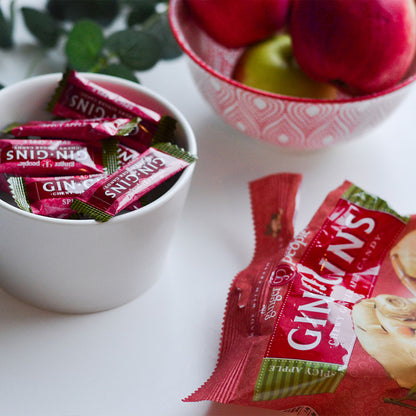 The Ginger People Gin Gins Chewy Ginger Apple Candy in a cup with a bowl of red apples