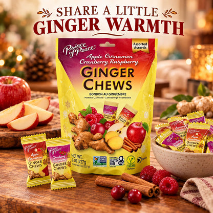A bag of Prince of Peace Ginger Chews surrounded by loose candies, sliced apples, cinnamon sticks, and fresh raspberries on a rustic wooden table, with the headline 'SHARE A LITTLE GINGER WARMTH' above.