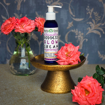 Herb Stop Goddess Glow Cream bottle on a gold stand with pink roses against a floral-patterned background