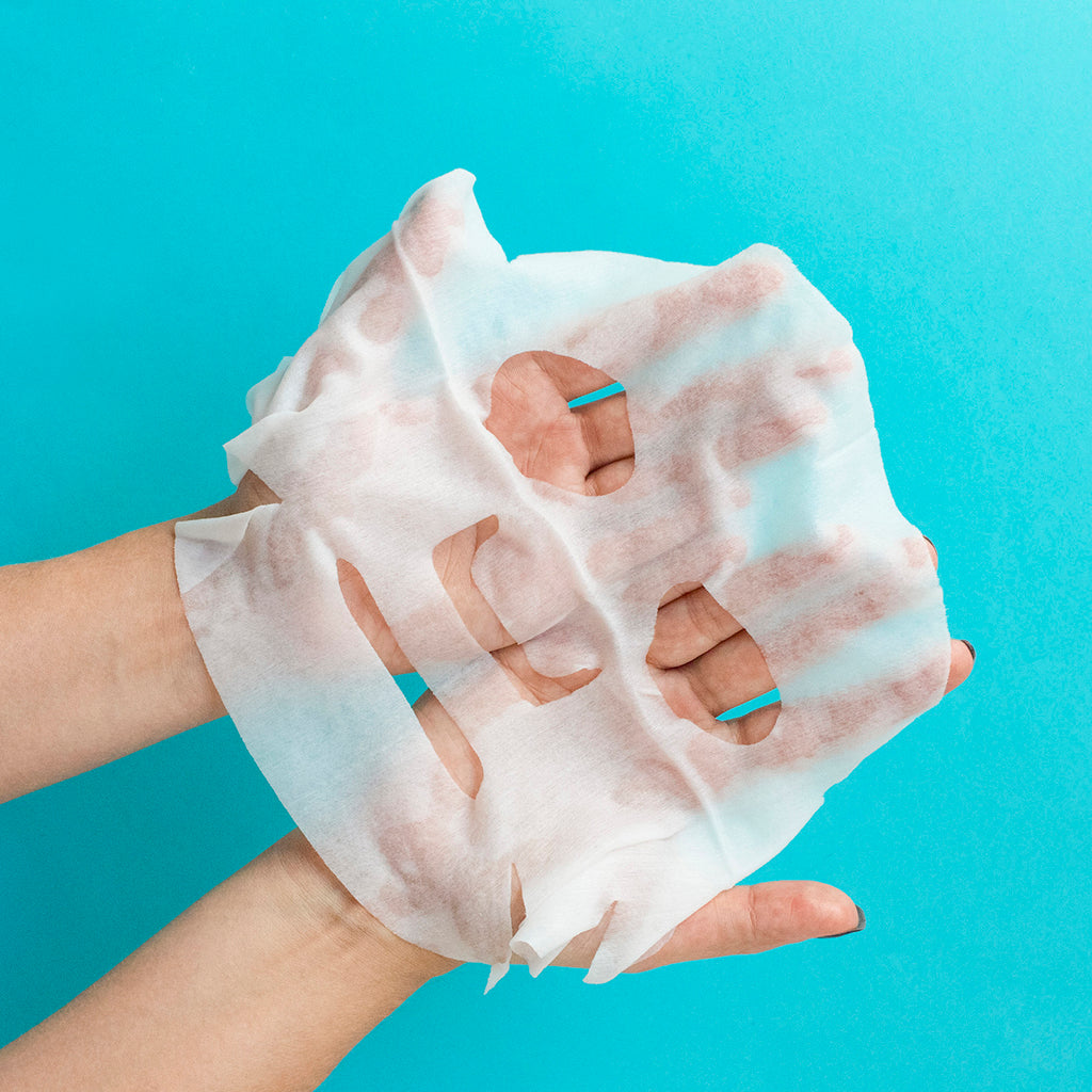 Hands holding a hyaluronic sheet face mask against a blue background