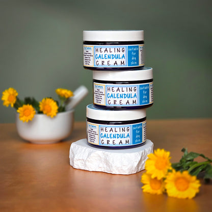 Stack of Herb Stop Healing Calendula Cream jars on a stone block with calendula flowers in the background.