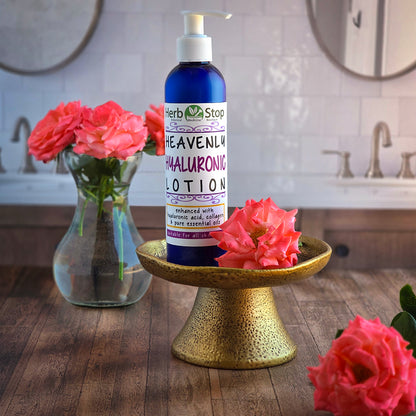 Bottle of Herb Stop Heavenly Hyaluronic Lotion on a gold stand with pink roses in a bathroom setting.