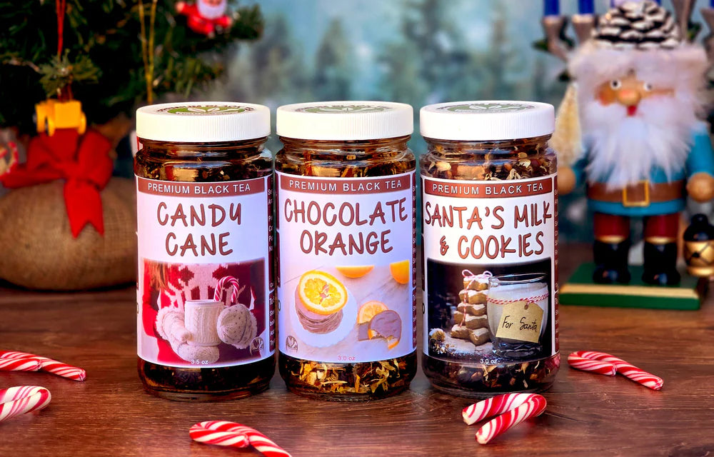 Three jars of premium black tea with festive labels on a wooden surface, surrounded by candy canes and Christmas decorations.