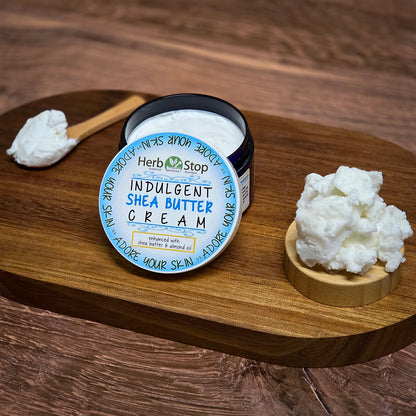 Jar of Herb Stop Indulgent Shea Butter Cream on a wooden surface with shea butter and a spoon.