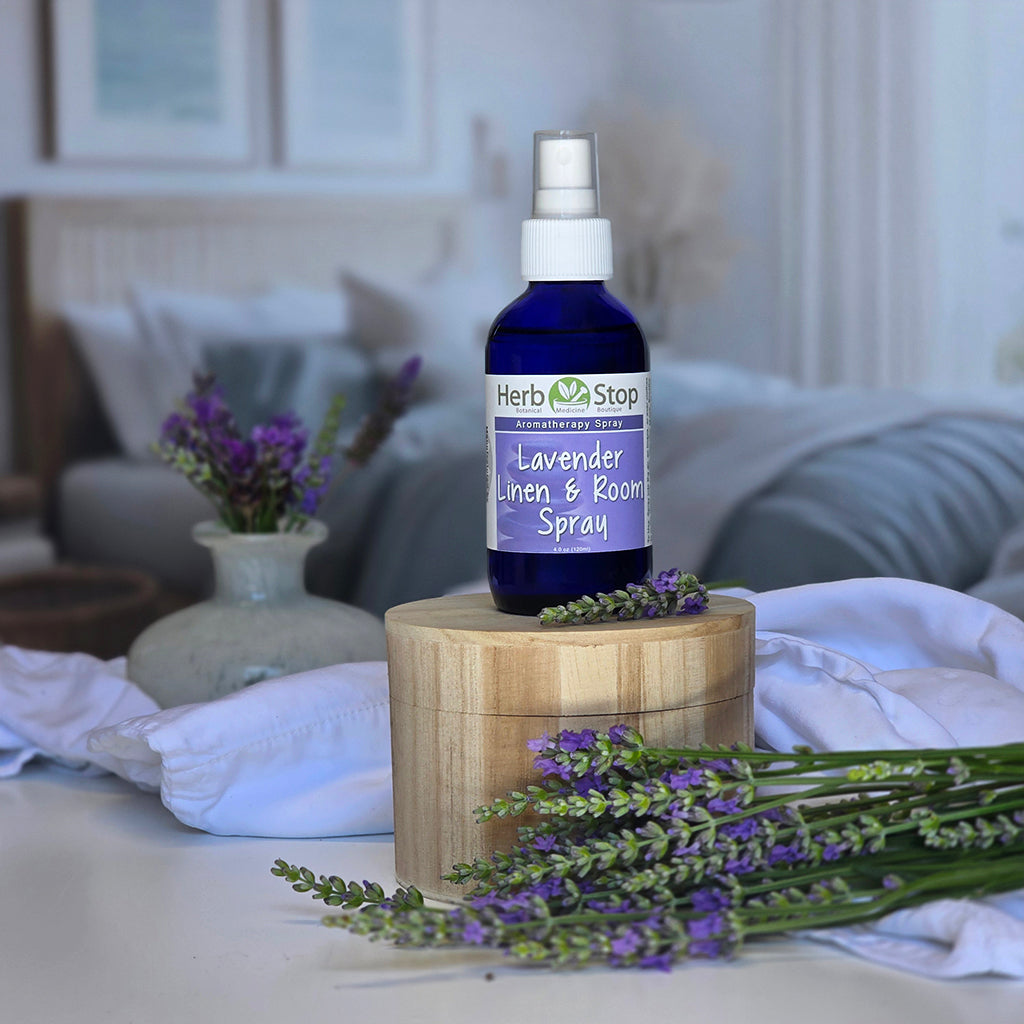 Herb Stop Lavender Linen & Room Spray bottle on a wooden block with lavender flowers in a room setting.