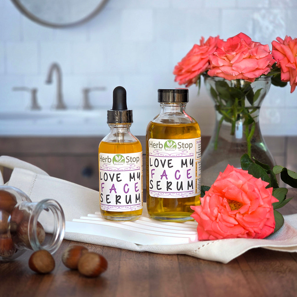 Two bottles of Herb Stop Love My Face Serum with roses and hazelnuts in a bathroom scene.