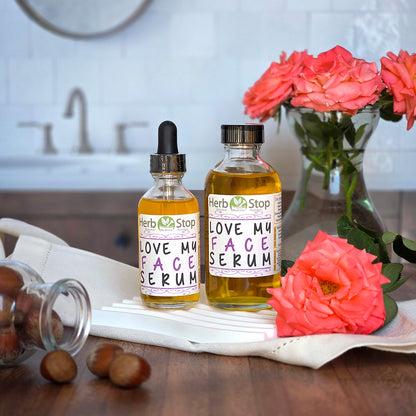 Two bottles of Herb Stop Love My Face Serum with roses and hazelnuts in a bathroom scene.