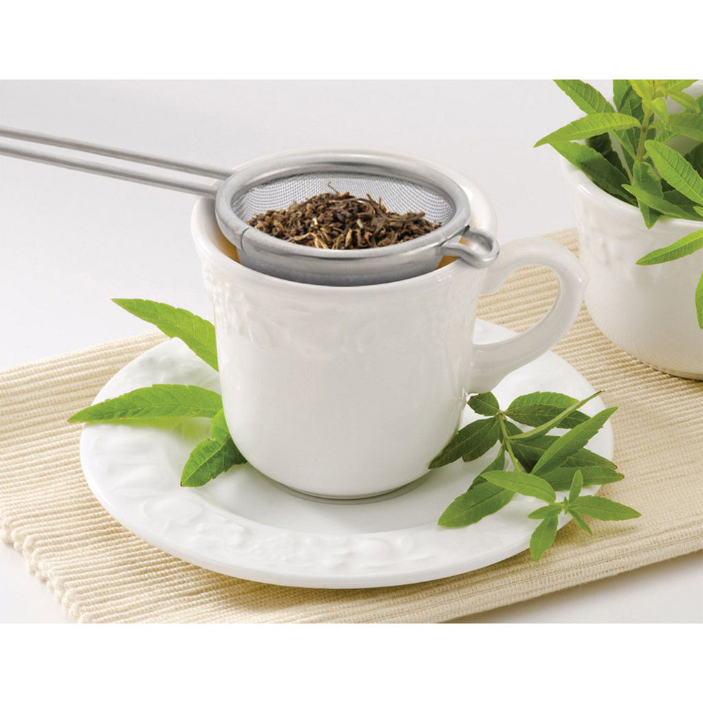 White tea cup with tea leaves and a strainer on a white background