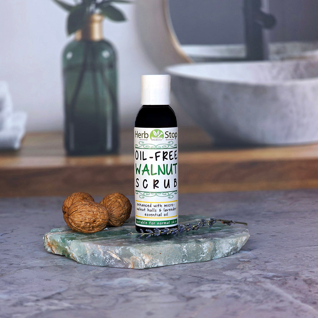 Bottle of Herb Stop Oil-Free Walnut Scrub on a fluorite slab with walnuts and a blurred bathroom background.