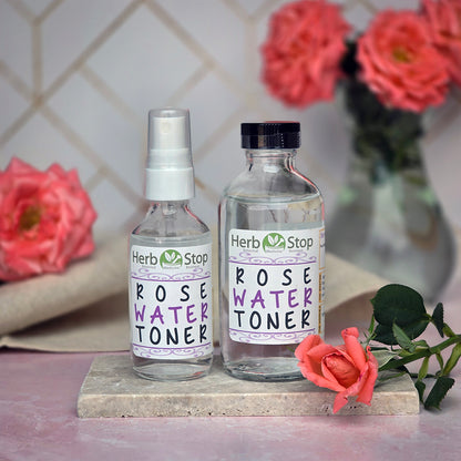 Herb Stop Rose Water Toner bottles on a pink surface with roses in the background