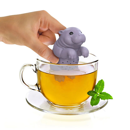 Hippo-shaped tea infuser being placed into a cup of tea with a hand holding it.