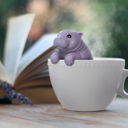 Hippo shaped tea infuser in a white cup with a book and lavender spring in the background
