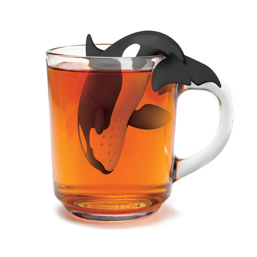 Tea infuser shaped like a whale in a glass of tea on a white background