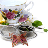 Tea ball with butterfly weight filled with tea next to tea cup