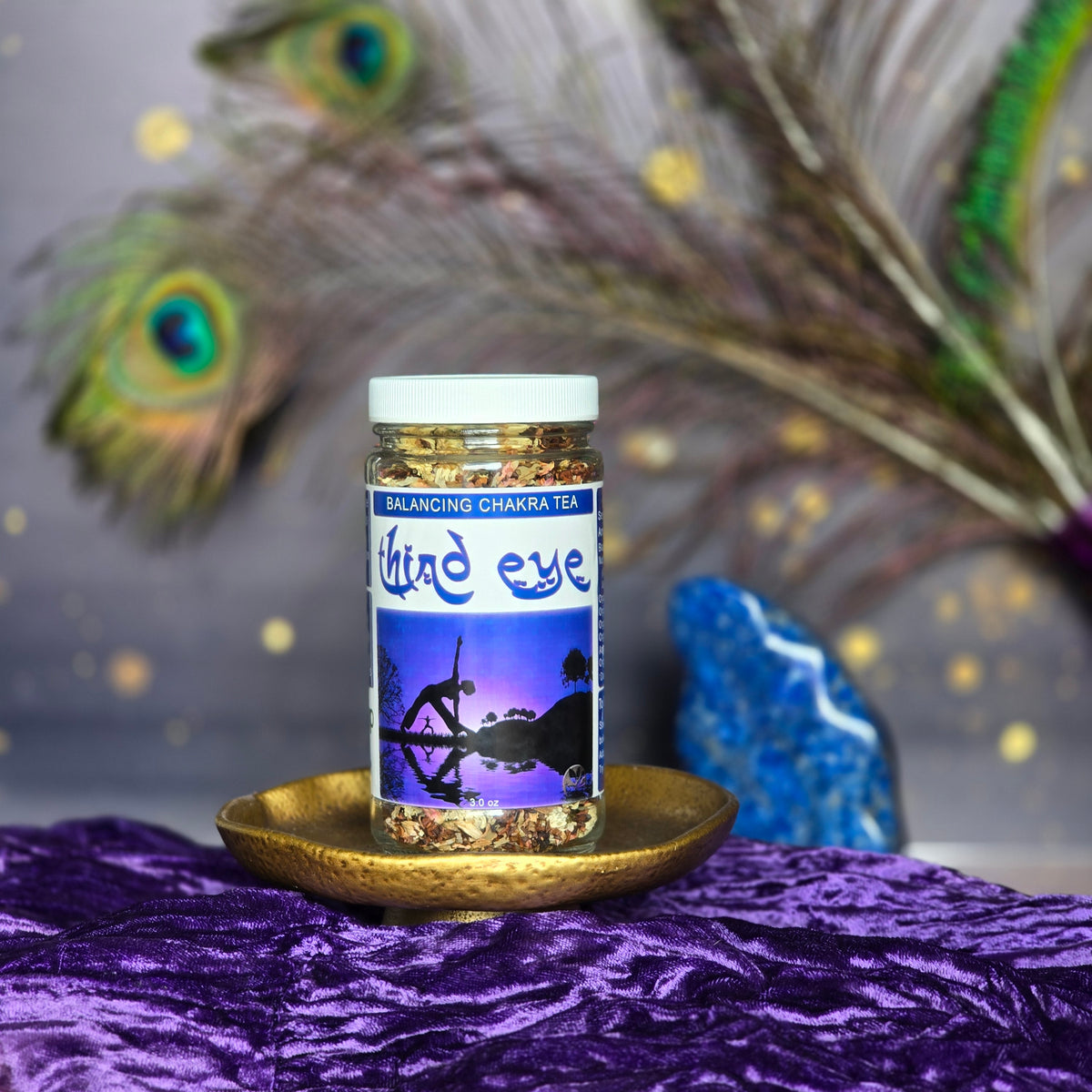 Third Eye Chakra Herbal Tea ion a purple velvet cloth with a blue stone and peacock feathers in the background