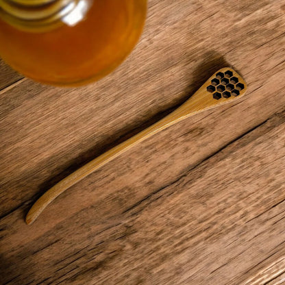 Bamboo honey dipper with honeycomb design on a wooden surface