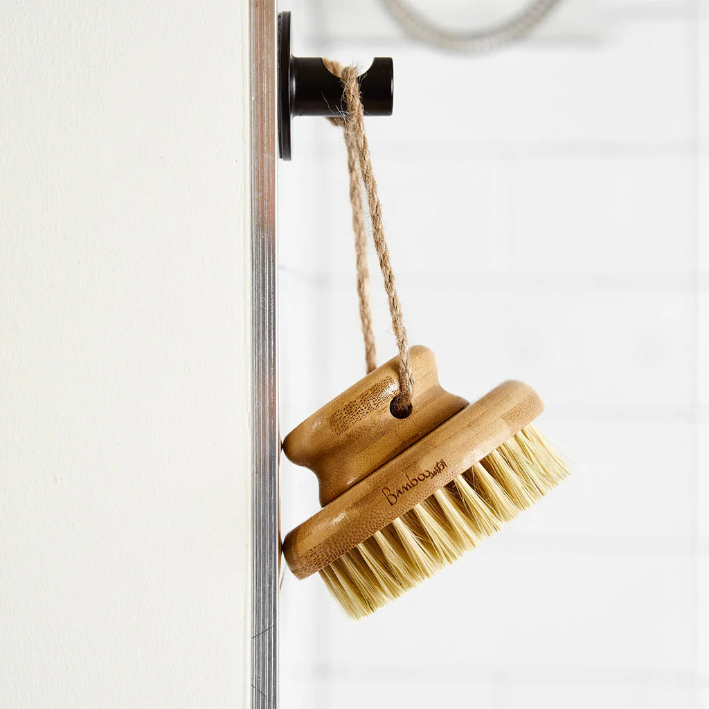 Bamboo brush with bristles hanging on a hook against a white background
