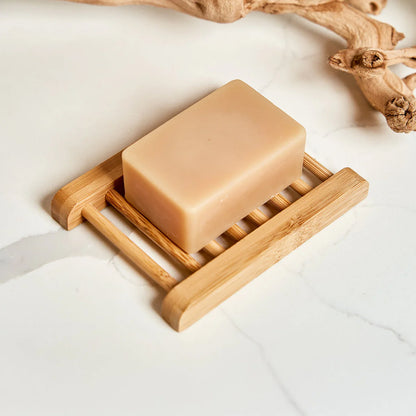 Bar of soap on a bamboo soap dish with natural wood background