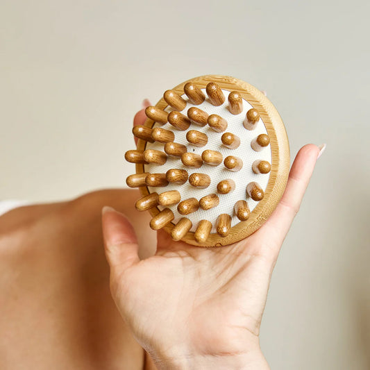 Hand holding a bamboo massage brush with a beige background