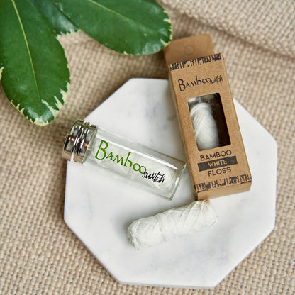 Bamboo switch dental floss bottle and packaging on a textured surface with leaves.