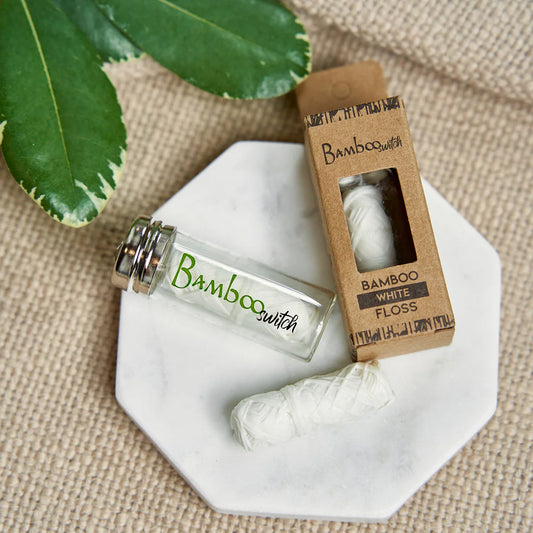 Bamboo switch dental floss bottle and packaging on a textured surface with leaves.