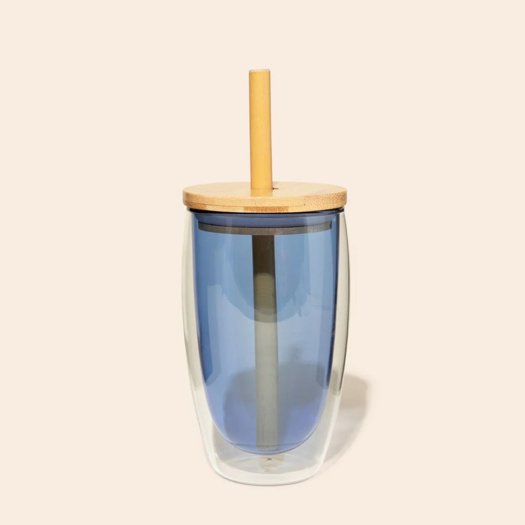 Blue double walled glass tumbler with a bamboo lid and straw on a beige background